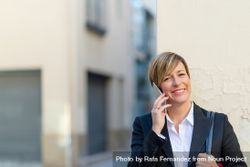 Smiling woman wearing a blazer and speaking on phone outside 4A17W4