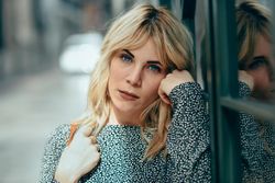 Close up of blonde female wearing casual clothes standing next to windows outside, copy space