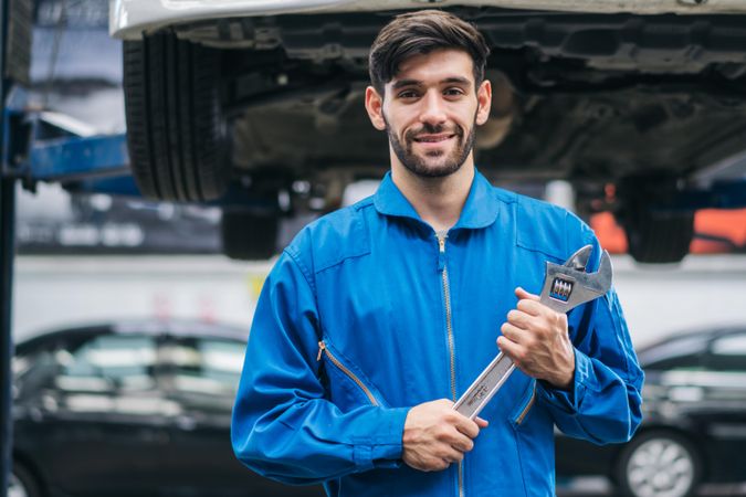 Smiling white male mechanic holding wrench at auto garage
