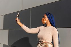 Stylish Black woman taking selfie in mask