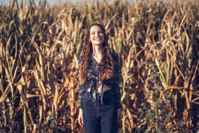 A Joyful Young Woman Standing in a Beautiful Cornfield During a Scenic Sunset Hour