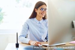 Happy woman in blue shirt working from monitor in her bright office 5pda85