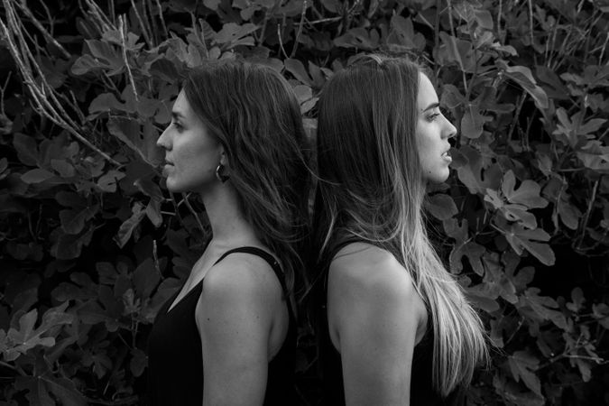 Young women posing near green bush