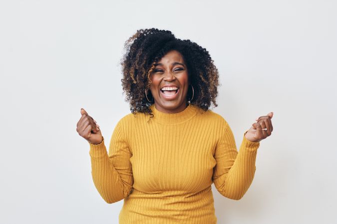 Studio shot of a excited Black woman in yellow shirt celebrating