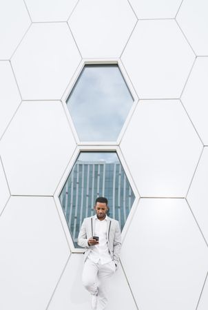 Elegant Black man browsing smartphone leaning on geometrical wall