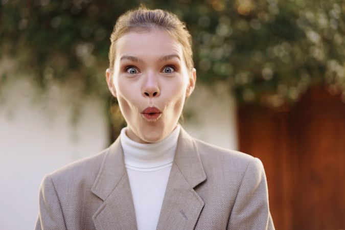 A surprised young woman joyfully expresses excitement outdoors, surrounded by nature