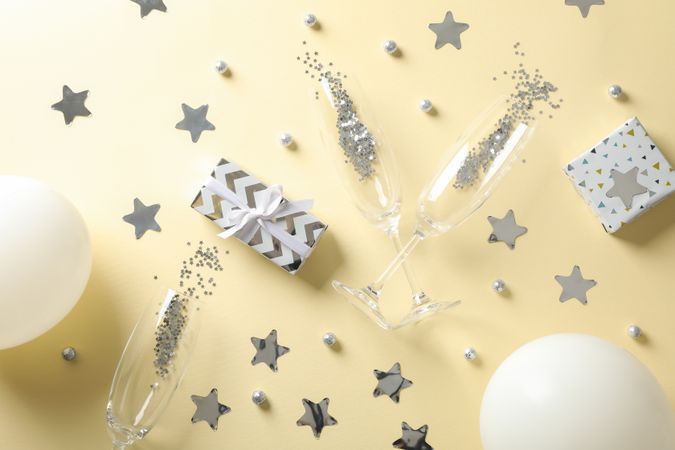 Composition with champagne glasses, gifts and glitter on beige background, top view