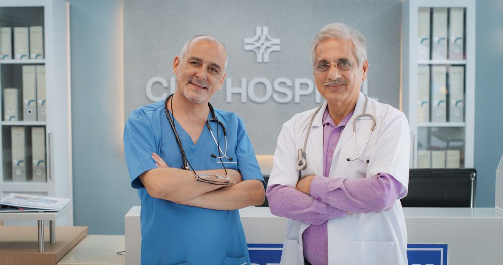Medical Hospital Medium Portrait: Two Friendly Indian Male Medical Doctors Crossing Their Hands, Looking at Camera and Smiling.