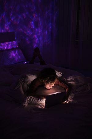 Boy surfing tablet in darkness