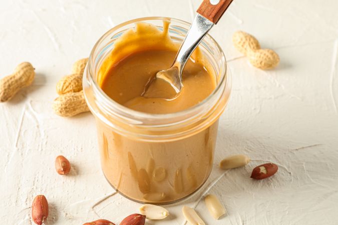 Glass jar with creamy peanut butter and spoon, and peanut on background, space for text and closeup