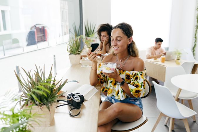 Stylish woman eating and reading book in cafe