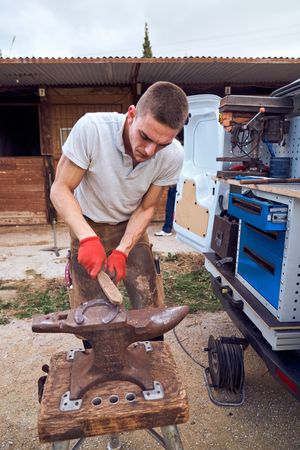 Blacksmith working on the anvil changing the horseshoe to a paw with tools