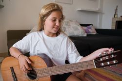 Cute girl sitting on floor while tuning wooden guitar