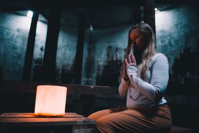 Woman with praying hands near lamp on bench in building