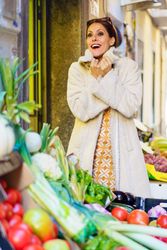 Smiling woman standing by colorful ripe fruits and vegetables in shop