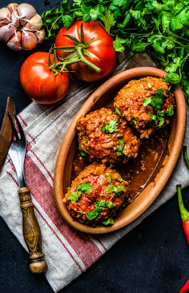 Three large meatballs served on table surrounded by fresh vegetables and herbs