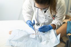 Young doctor with scissors and tweezers near hand of patient