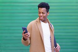 Happy Cuban male texting on his phone in front of green wall