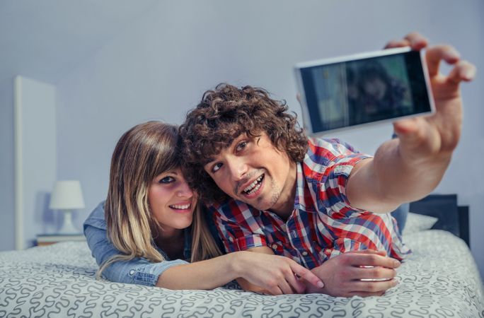 Couple taking selfie lying on top of bed