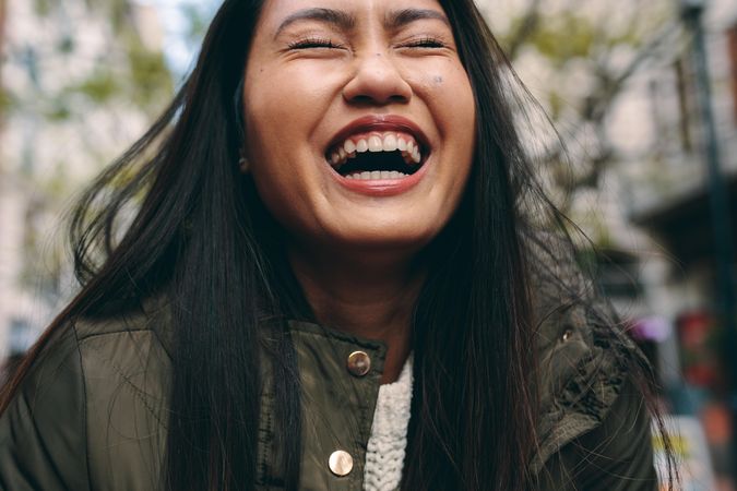 Close-up of young Asian woman laughing with eyes closed