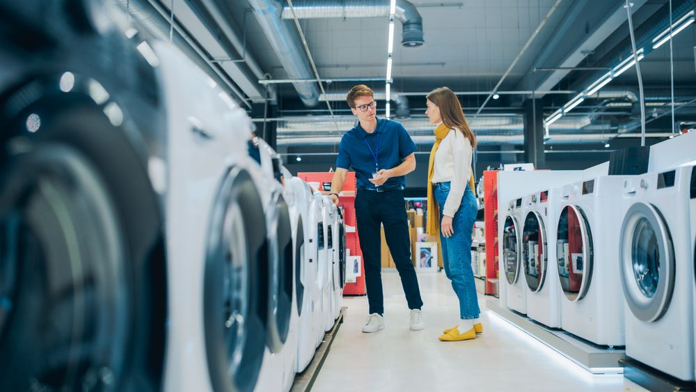 Young Female Customer Engages with Home Electronics Store Associate while Selecting a Washing Machine.
