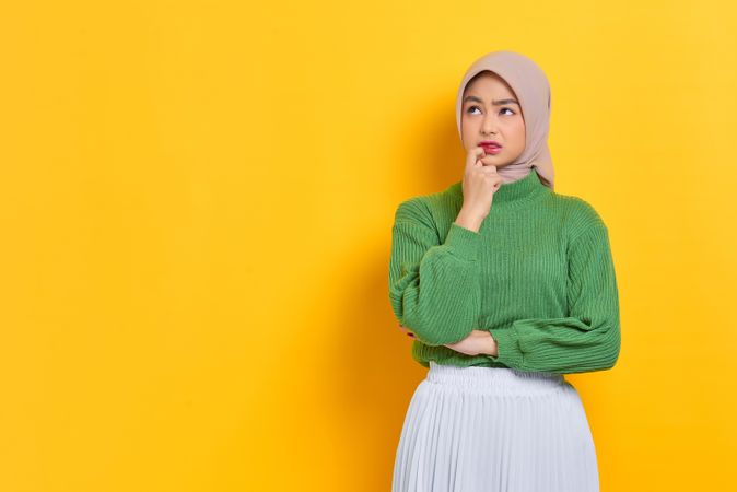 Woman in headscarf wondering about something with finger near mouth with copy space