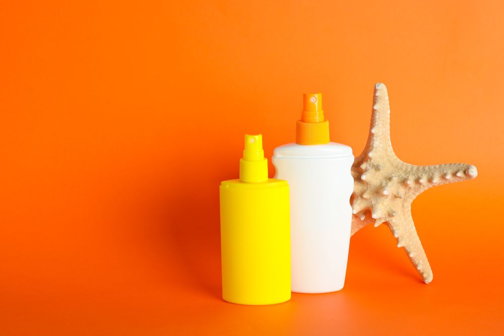 Sunscreen sprays with starfish on color background, space for text