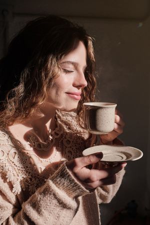 Young woman smelling aromatic cup of coffee