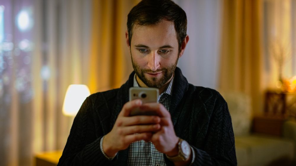 Portrait of a Man at Home Holding His Smartphone with Both Hands.