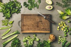 Arrangement of sliced green garden vegetables on concrete surface, with wooden board
