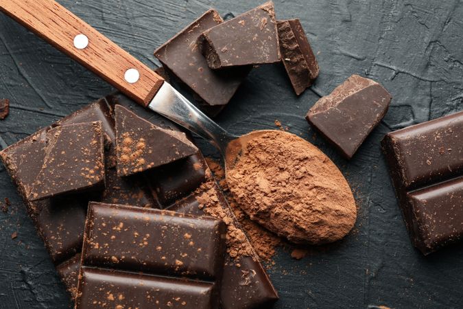 Tasty chocolate and spoon with powder on dark background