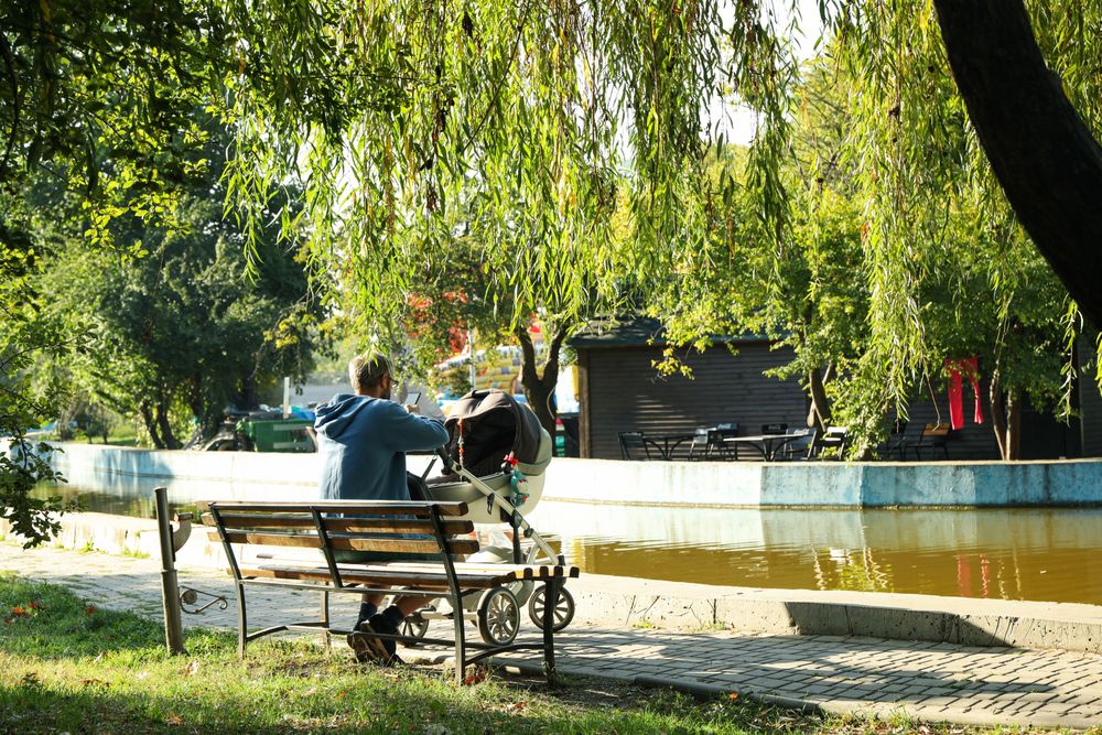 Man with stroller sitting on bench in city park