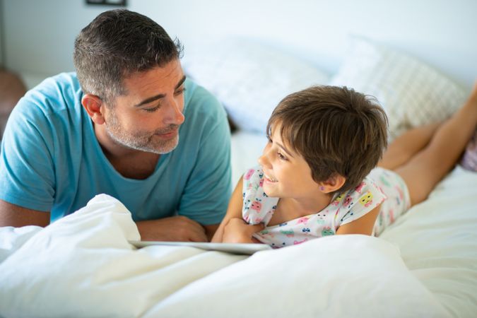 Dad with child playing on tablet in bed