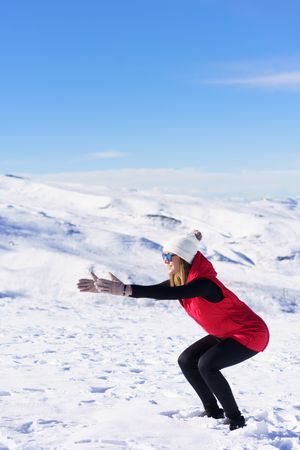 Woman in winter gear doing squats on snowy mountain