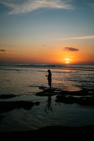 Side view of man fishing on Bali beach at sunset