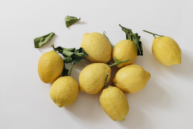 Fresh yellow lemons, dry green leaves on table