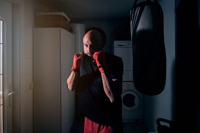 Man training boxing in the laundry room at home with a bag