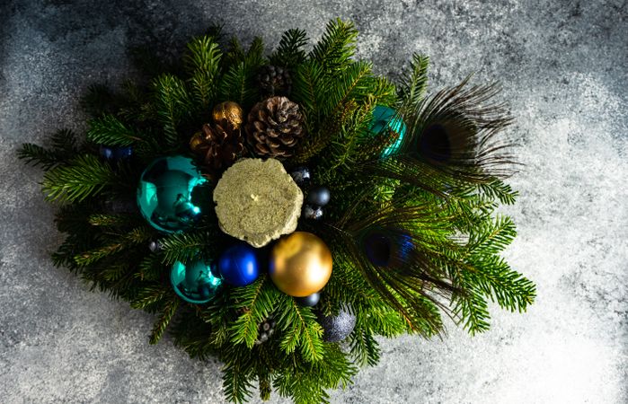 Top view of blue and gold Christmas decorations in pine centerpiece with candle and peacock feathers