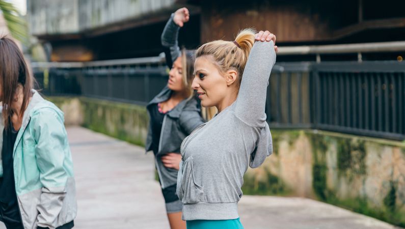 Woman runner stretching arms next to her female friends before training