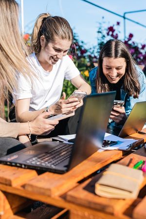 Young women smiling showing videos or news on their mobiles on a break from work outside the office.