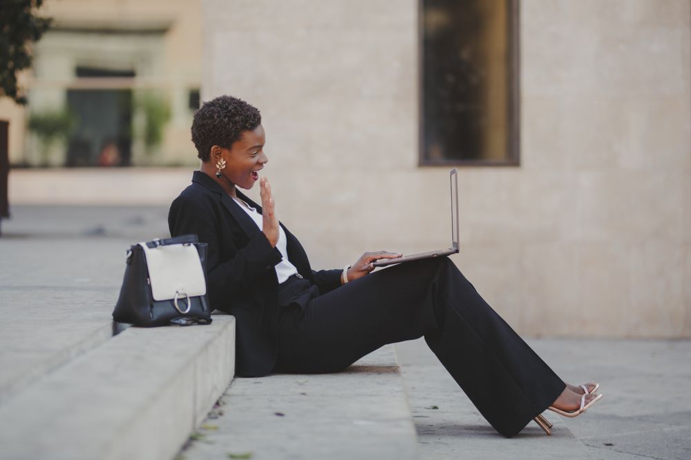Stylish Black woman with laptop on steps near handbag