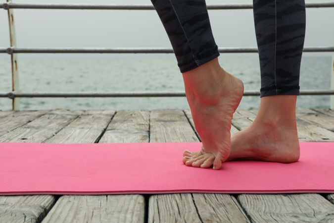 Female feet on pink yoga mat on wooden floor outdoors, close up