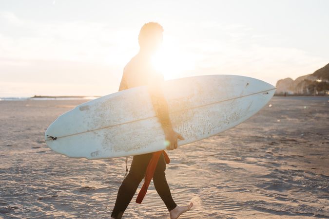 Tattooed man with surfboard under his arm at sunset