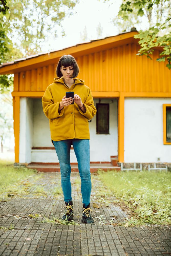Smiling woman using smartphone near countryside house