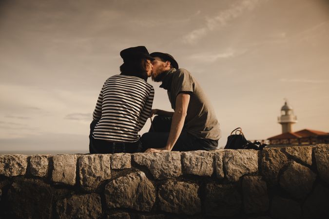 Man kissing woman on stones near lighthouse