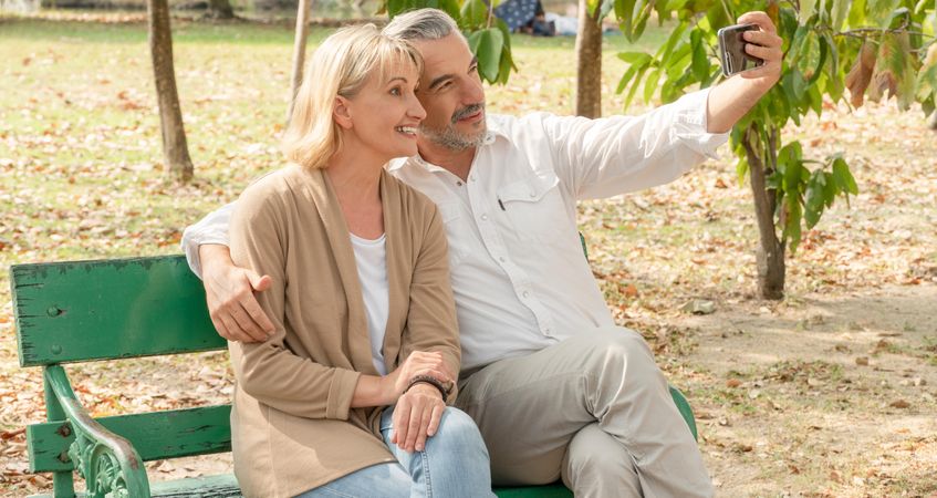 Male and female older couple taking selfie together on park bench