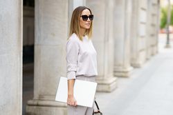 Chic woman in grey walking outside with laptop