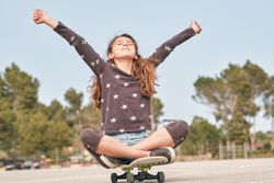 Excited girl sitting with outstretched arms on skateboard