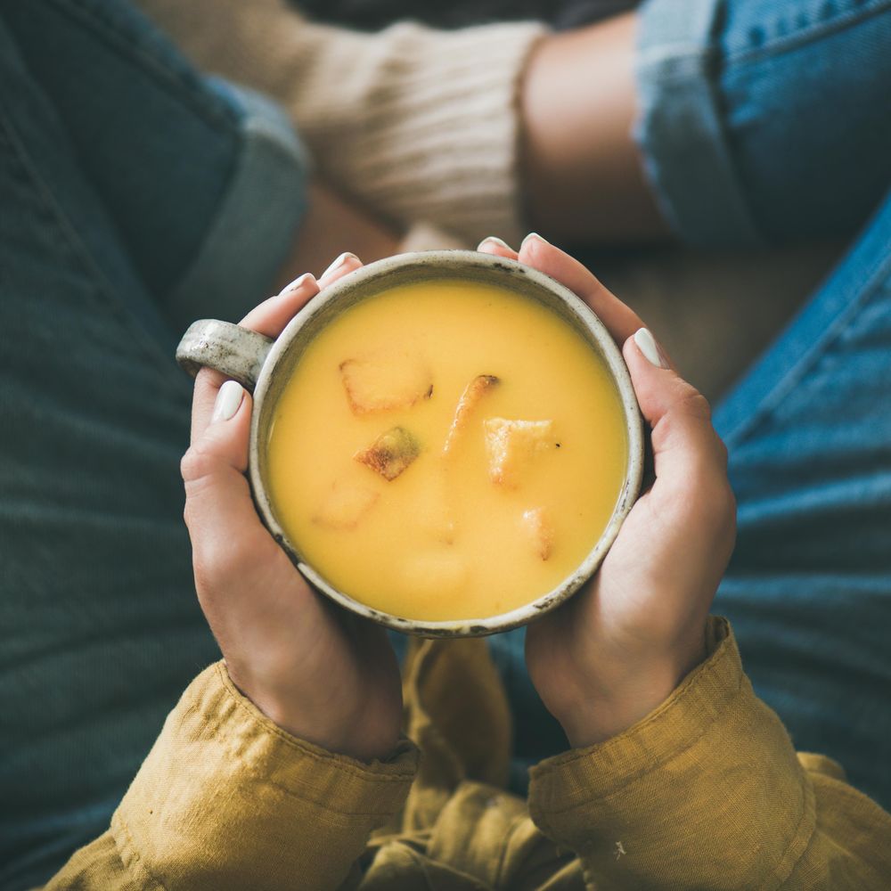 Woman in jeans holding cup of squash soup, square crop