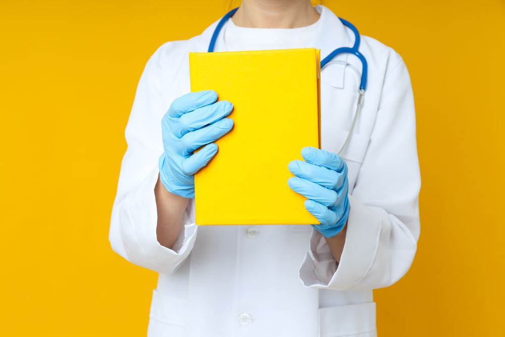 Female doctor holds yellow book on yellow background